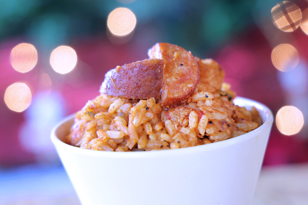 A close up of a beautiful little bowl of jambalaya fresh off the buffet. There are Christmas lights in the background and hints of red and green.